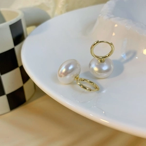 Elegant French style gold hoop earrings with white freshwater pearls on a white plate
