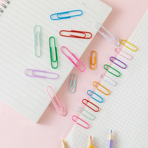 Colorful macaron paper clips scattered on a notebook with stationery items on pink background