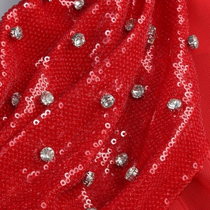 Detail of red sequined evening dress fabric with silver claw-set rhinestones and pleats
