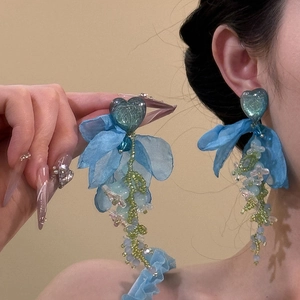 Detail of long heart-shaped tassel earrings with blue chiffon and beadwork on a model