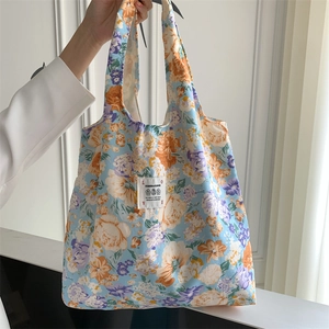 Dettaglio della borsa tote in tela floreale con base blu, fiori arancioni e etichetta