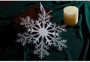Close-up of a large clear acrylic snowflake ornament with a purple string on green fabric
