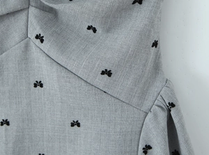 Detail of light gray twill fabric featuring black 3D butterfly embroidery and pleats