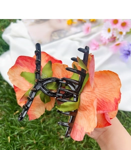 Detailed close-up of a floral hair claw clip featuring large orange-pink gradient rose petals