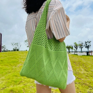 Detail of green knit tote bag with diamond pattern shown on model outdoors