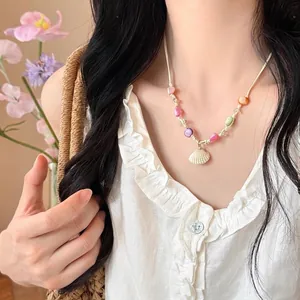 Detail of seashell pendant necklace with colorful beads and beige woven rope on a model
