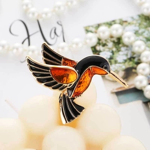 Elegant gold-tone hummingbird brooch with black enamel wings on pearl background