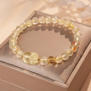 Detailed shot of yellow quartz beads with golden Pixiu and coin charm on a jewelry box