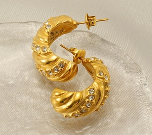 Détail macro de boucles d'oreilles C en or 18k avec texture spirale et oxydes de zirconium