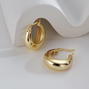 Polished thick gold hoop earrings on minimalist white stone sculpture display