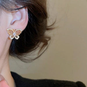 Macro view of gold plated butterfly stud earring with zircon inlay on model ear