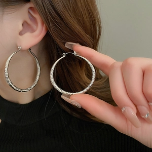 Detailed view of silver hoop earrings with hammered metal texture on model's ear
