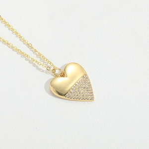 Macro shot of gold heart pendant with half-paved rhinestones on white texture