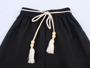 Dettaglio dei pantaloni neri con elastico in vita e cordino intrecciato con perline