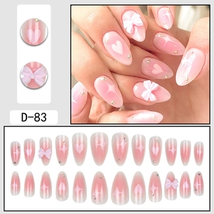 Pink gradient almond press-on nails with heart patterns, white bows and tiny rhinestones