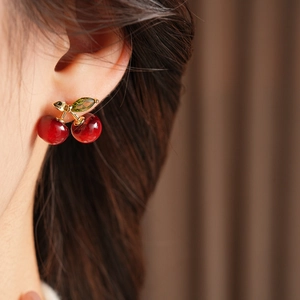 Close-up of red resin cherry earrings with golden stems and green crystal leaf on ear