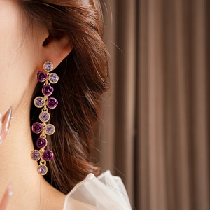 Détail de boucles d'oreilles pendantes dorées avec roses violettes et cristaux