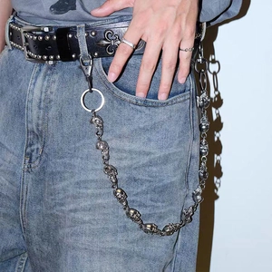 Detail of silver skull metal pants chain on denim jeans with studded leather belt
