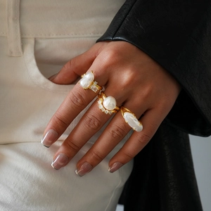 Detailed macro view of baroque pearl gold rings with zircon stones on model's hand
