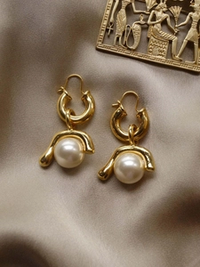 Detail of large white pearls on golden rings over elegant beige silk fabric background