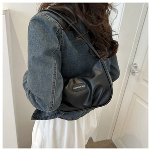 Side view of a black pleated crescent underarm bag worn by a model in casual attire
