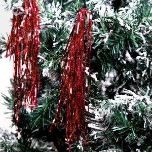 Close-up of red metallic tinsel on a snow-flocked Christmas tree branch for holiday decor