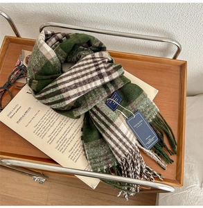 Detail of green and white plaid cashmere feel scarf with fringes on a wooden tray