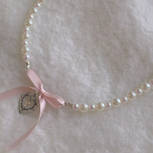 Detail of pearl necklace with a pink ribbon bow and silver heart cross pendant