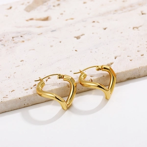 Close-up of golden heart-shaped twisted hoop earrings on a natural stone base