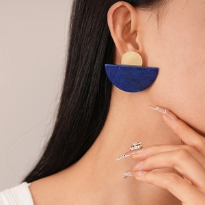 Close-up of model wearing geometric blue resin and gold metal semi-circle earrings