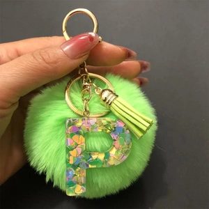 Detail of green pompom keychain with clear resin letter P and heart-shaped sequins
