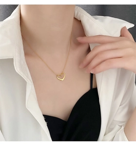 Close-up of a gold hollow heart pendant necklace worn by a model on a white shirt
