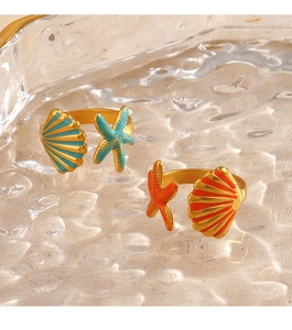 Close-up of golden starfish and seashell open rings with enamel on a glass tray
