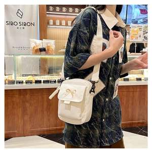 Close-up of white canvas crossbody bag with brown bow embroidery in a cafe setting