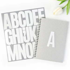 Detailed view of white 3-inch waterproof alphabet stickers on a grey grid notebook