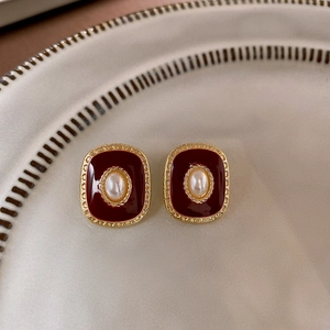 Detail of red square earrings with imitation pearl and gold textured edge on a ceramic tray