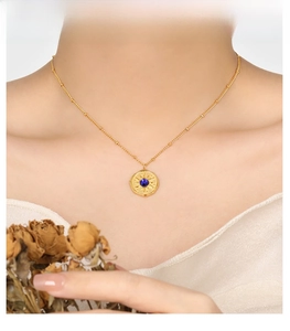 Close-up of gold sunburst necklace with blue stone on neck with floral accents