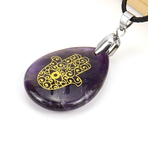 Macro shot of purple amethyst water-drop pendant with golden Hamsa Hand engraving