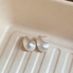 Macro detail of silver-tone teardrop earrings featuring a matte brushed texture finish
