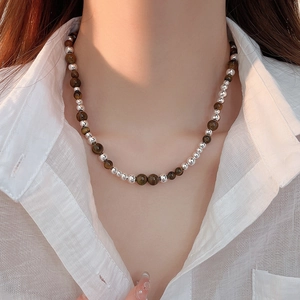 Close-up of tiger eye and silver bead necklace worn by a model in a white shirt