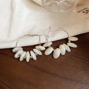 Close-up of silver hoop earrings with cream resin beads on rustic wooden and linen background