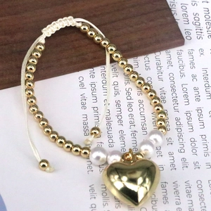 Macro detail of adjustable hand-woven bracelet with gold heart charm and white pearls