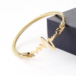 Macro shot of 18k gold heartbeat EKG charm on twisted cable stainless steel bangle