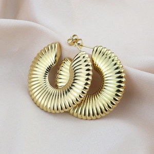 Macro detail of golden C-shaped hoop earrings with vertical ribbed texture on pink silk