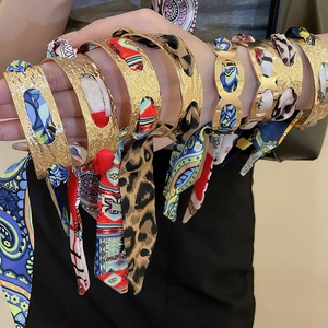 Close-up of gold hammer-texture bangles wrapped with vibrant leopard and floral silk scarves
