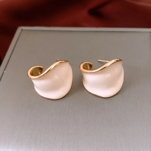 Detail of C-shaped cream enamel earrings with wavy gold-plated edges on red silk cloth