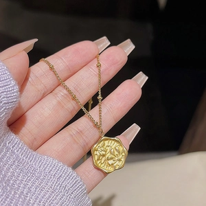 Close-up of golden stainless steel butterfly necklace with floral embossed round pendant