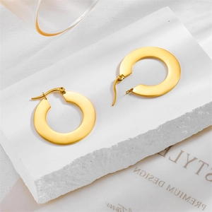 Minimalist gold-tone wide round hoop earrings displayed on a white textured stone base