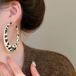 Detail of model wearing large cow print resin hoop earrings with black and white patterns
