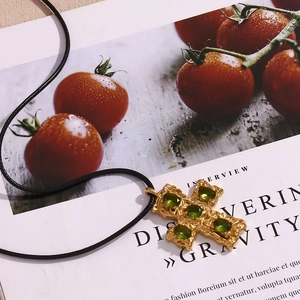 Detail of 18K gold-plated hammered cross pendant with green emerald-like gems on black cord
